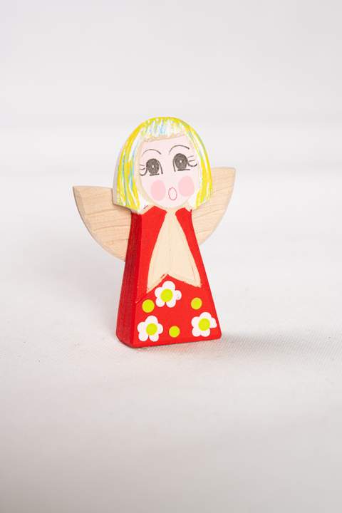 Drewniany anioł, duży, zczerwonym tułowiem w białe kwiatki z żółtymi kropkami włosy żółto niebiesko białe