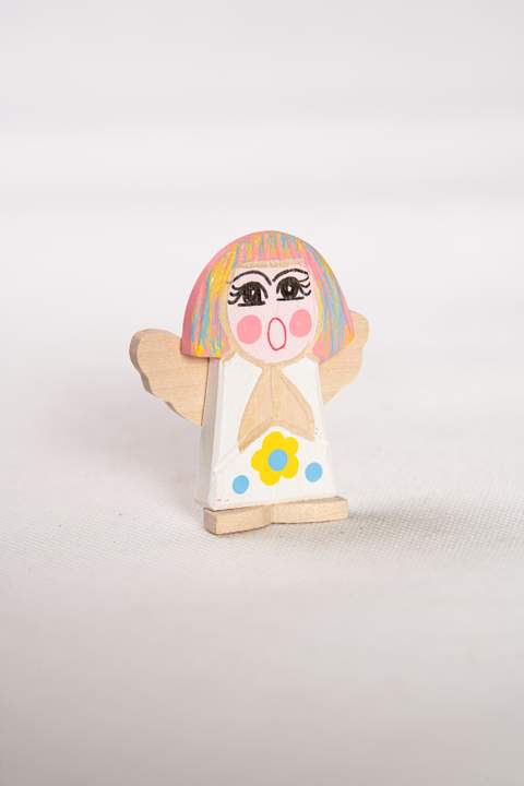 Drewniany anioł, mały, z białym tułowiem z żółtym kwiatkiem z niebieskimi kropkami, włosy w kolorze różowym żółtym i niebieskim