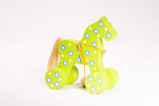 Koń na kólkach z drewna, w kolorze jasnej zieleni, w błękitne kwiaty i białe kropki, z żółtym sznurkiem