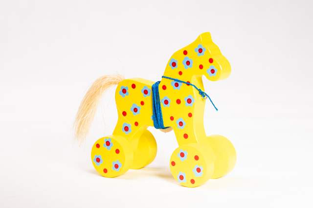 Drewniany koń na kólkach, żółty, w błękitne kwiatki  i wyraźne czerwone kropki, z niebieskim sznurkiem owiniętym wokół tułowia