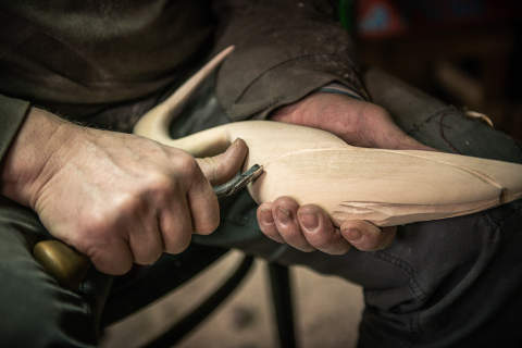 Ręce osoby rzeżbiącej dłutem w kawałku drewna przypominającym ptaka